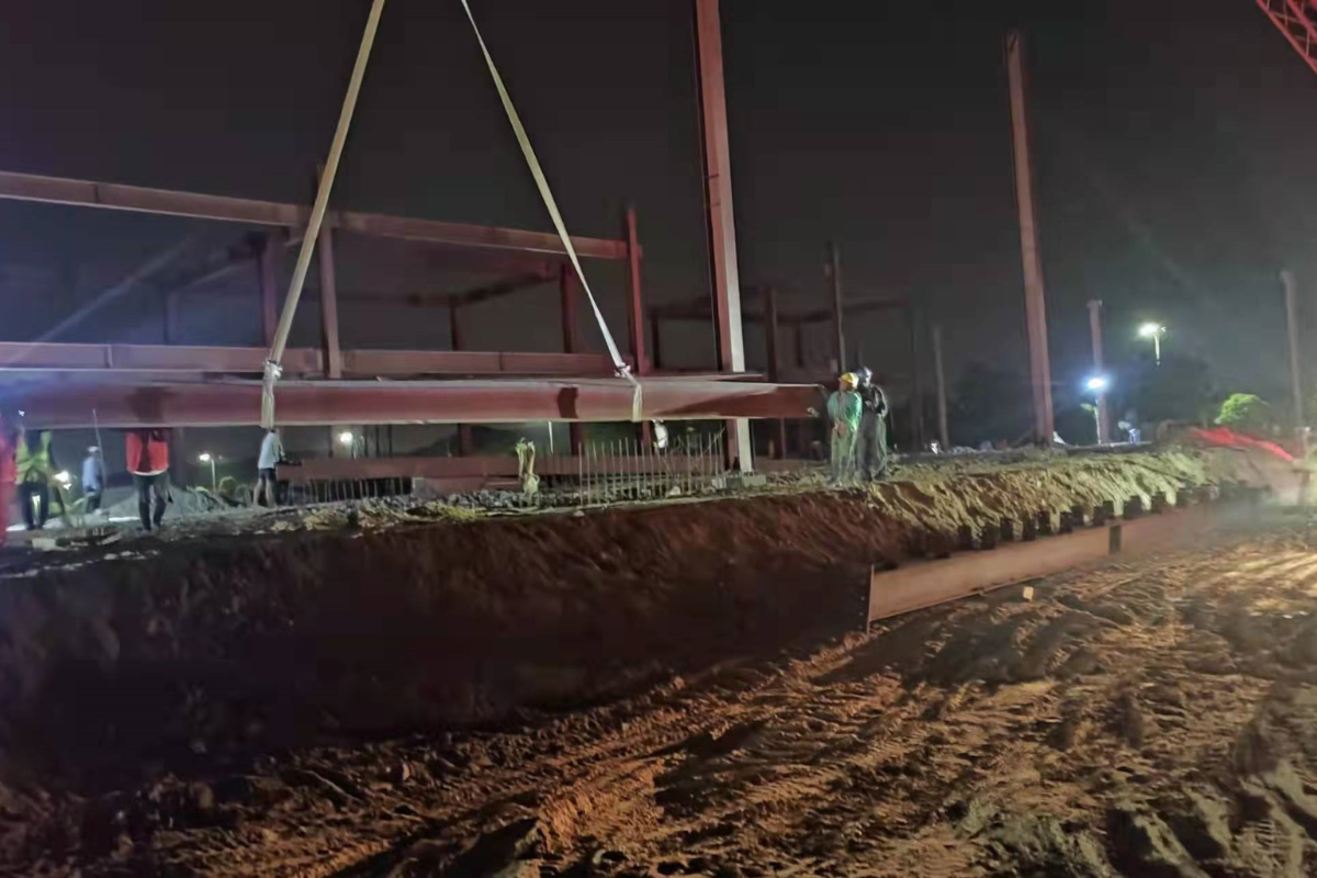 Night construction scene at Emerald E-Commerce Center in Naypyidaw, Myanmar, with a crane lifting a large steel beam for super structure erection.